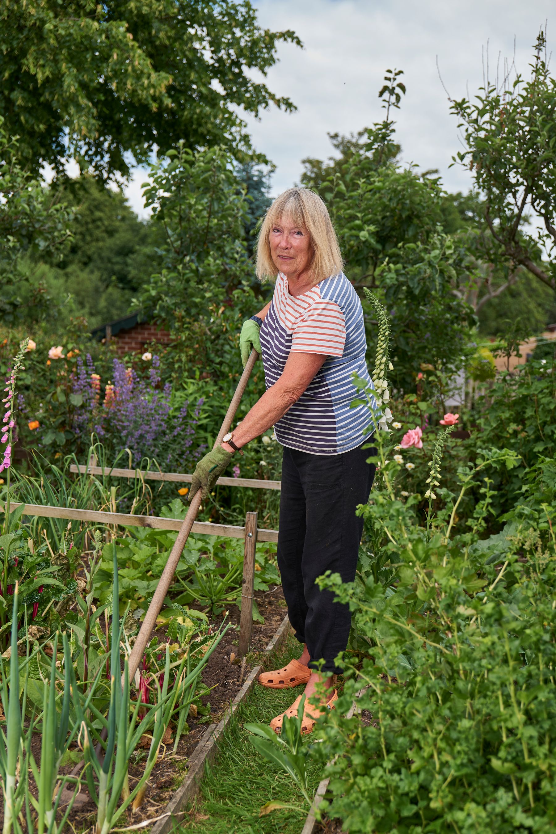 An older woman tending a small, flower-filled garden plot
